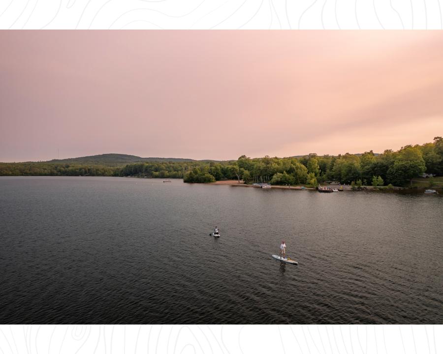 两个人站在桨板上越过平静的独立湖在日落大湾，密歇根州