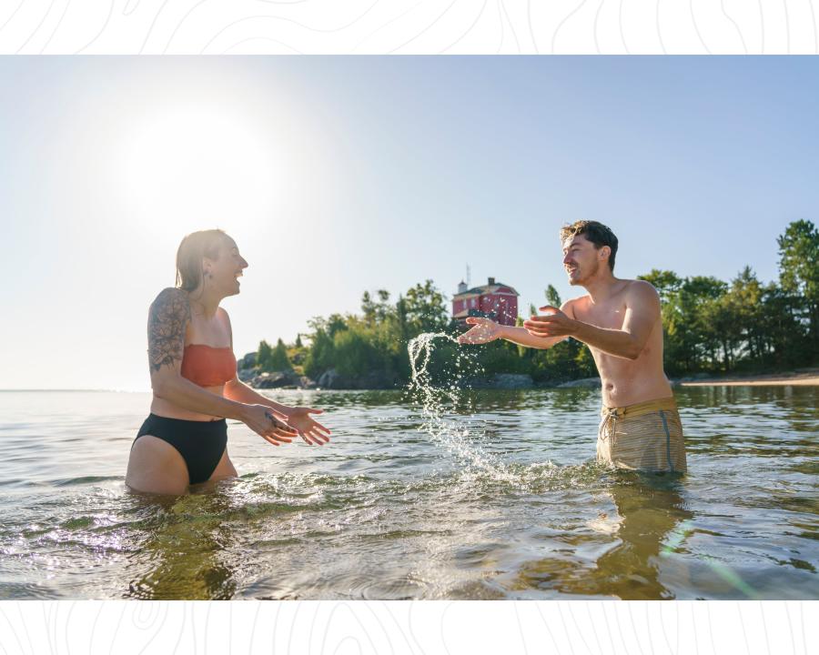 一对情侣在苏必利尔湖游泳, 在历史悠久的红色海港灯塔前互相泼水, MI