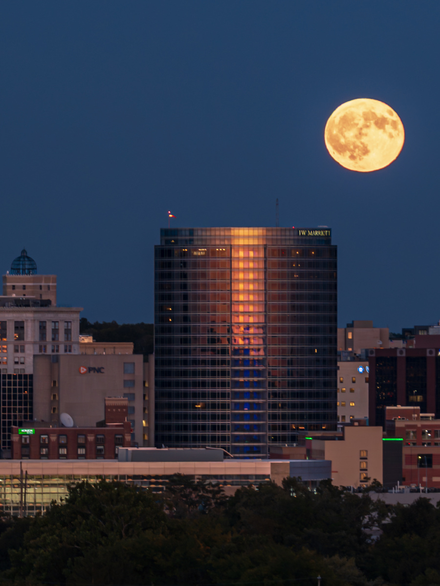 Full moon rising above illuminated buildings in the downtown Grand Rapids skyline.