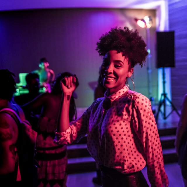Woman dancing, amidst other dancers, at a dim club.