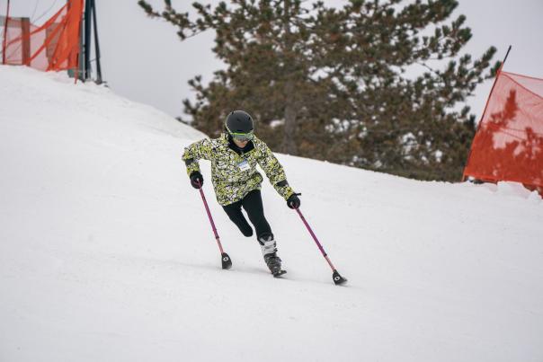 Woman skiing downhill on one ski and two "outriggers" - poles with skis on the bottom of them. http://wp.skiccsa.org/