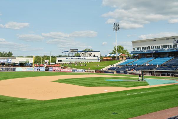A baseball stadium used by the West Michigan Whitecaps, with a well-manicured field, surrounded by bleachers and a clear blue sky with scattered clouds.