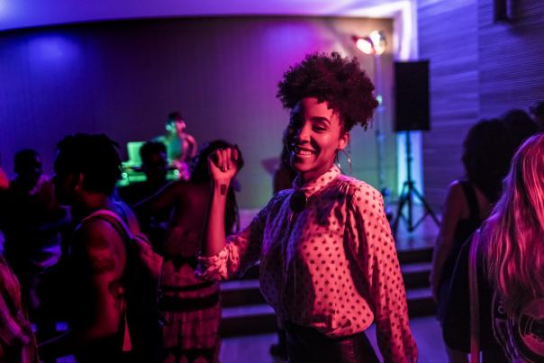 Woman dancing, amidst other dancers, at a dim club.