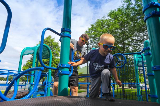 Father observing son play on playground equipment on a sunny day