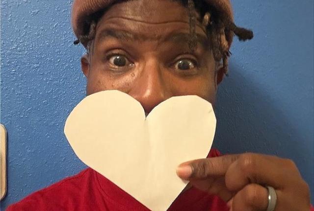 A guy with a hat on holding up a paper heart