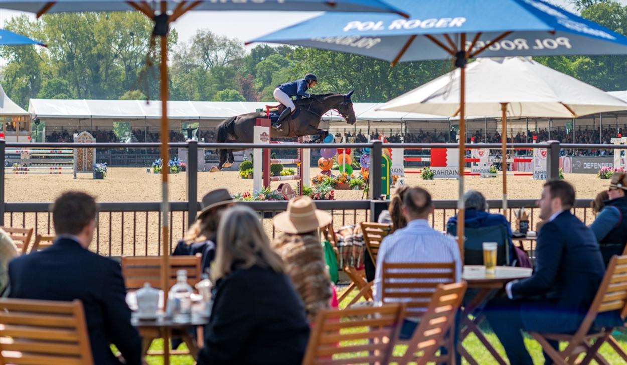 Royal Windsor Horse Show - people at tables under parasols watching showjumping