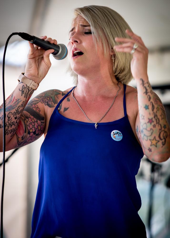 Woman with tattoos in a blue shirt with a LoCo sticker singing into a mic at 868 Estate Vineyards
