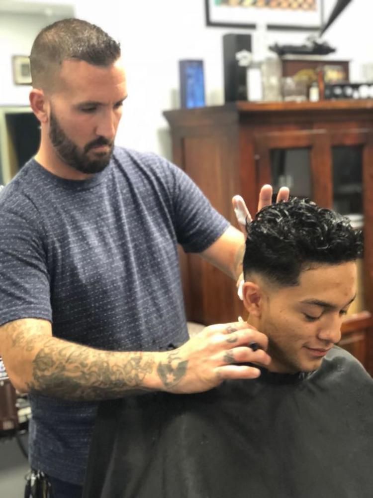 One man cuts another man's hair as he sits in a chair