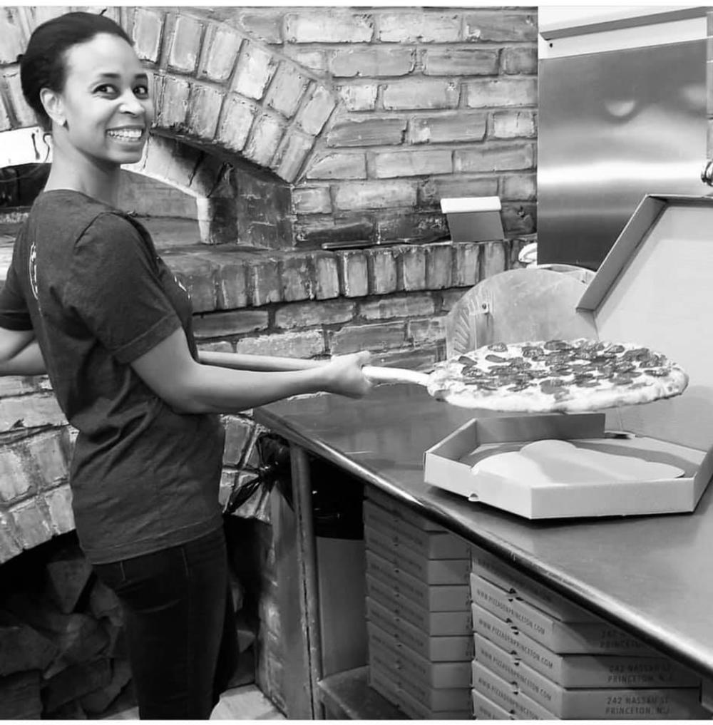 Smiling employee prepares a pepperoni pizza at Pizza Den
