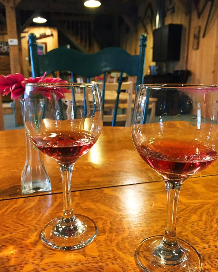 Two glasses of red wine on a wood table with red flowers