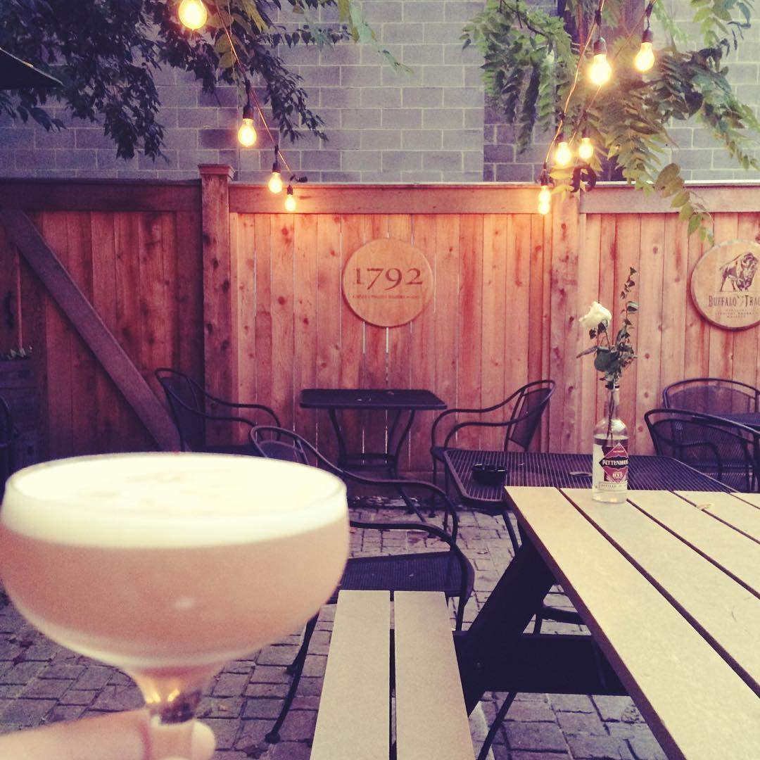 Bourbon cocktail held up with wood and brick patio and string lights in the background