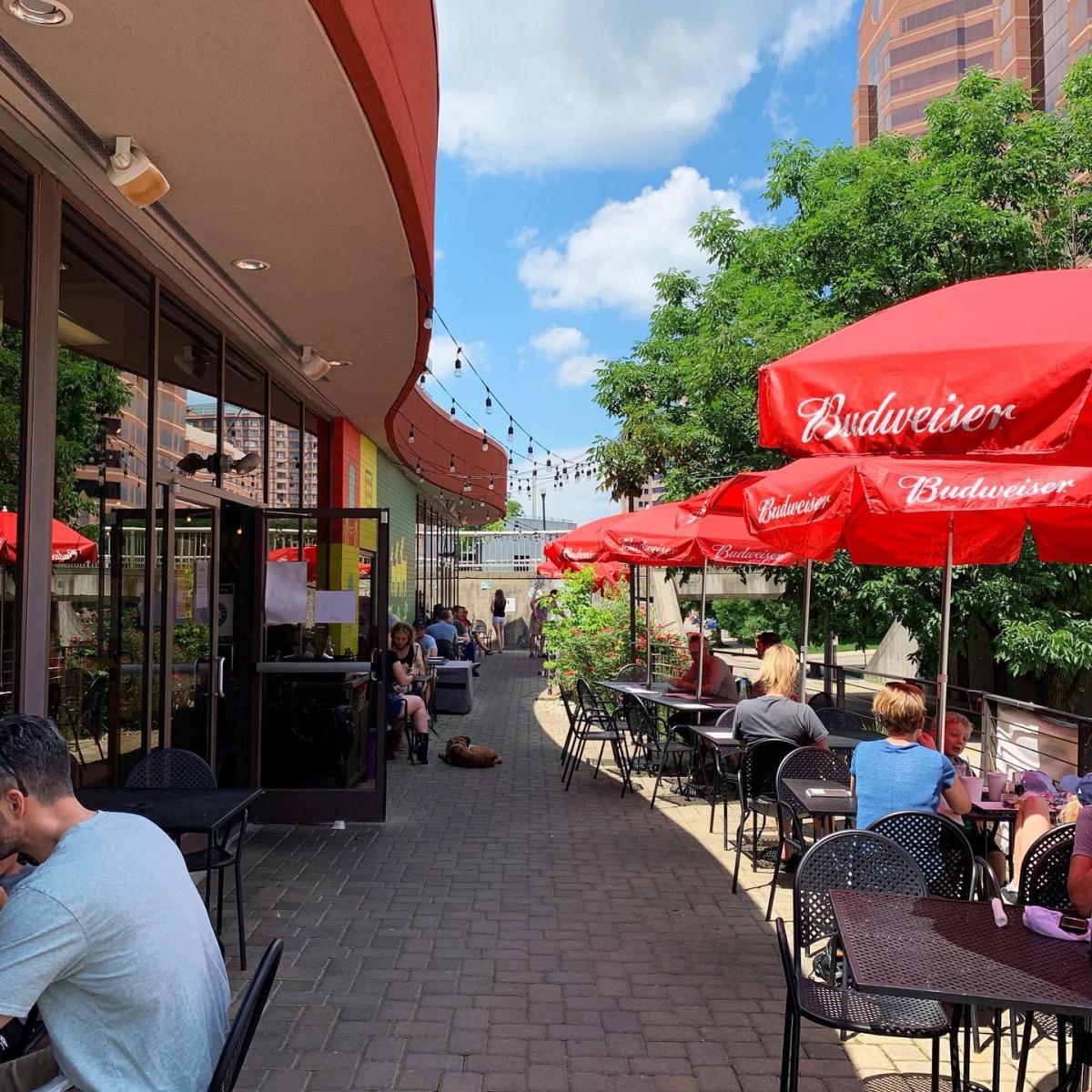 red umbrellas and black outdoor patio tables on a brick sidewalk in front of the gruff in covington ky