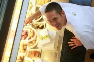 Pistacia Vera owner and chef Spencer Budros leaning into display case of pastries while wearing white chef coat