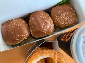 Boxful of hamburgers next to onion rings and cup of soda from Burgerim