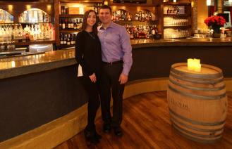 A woman and man standing together in front of a wine bar.