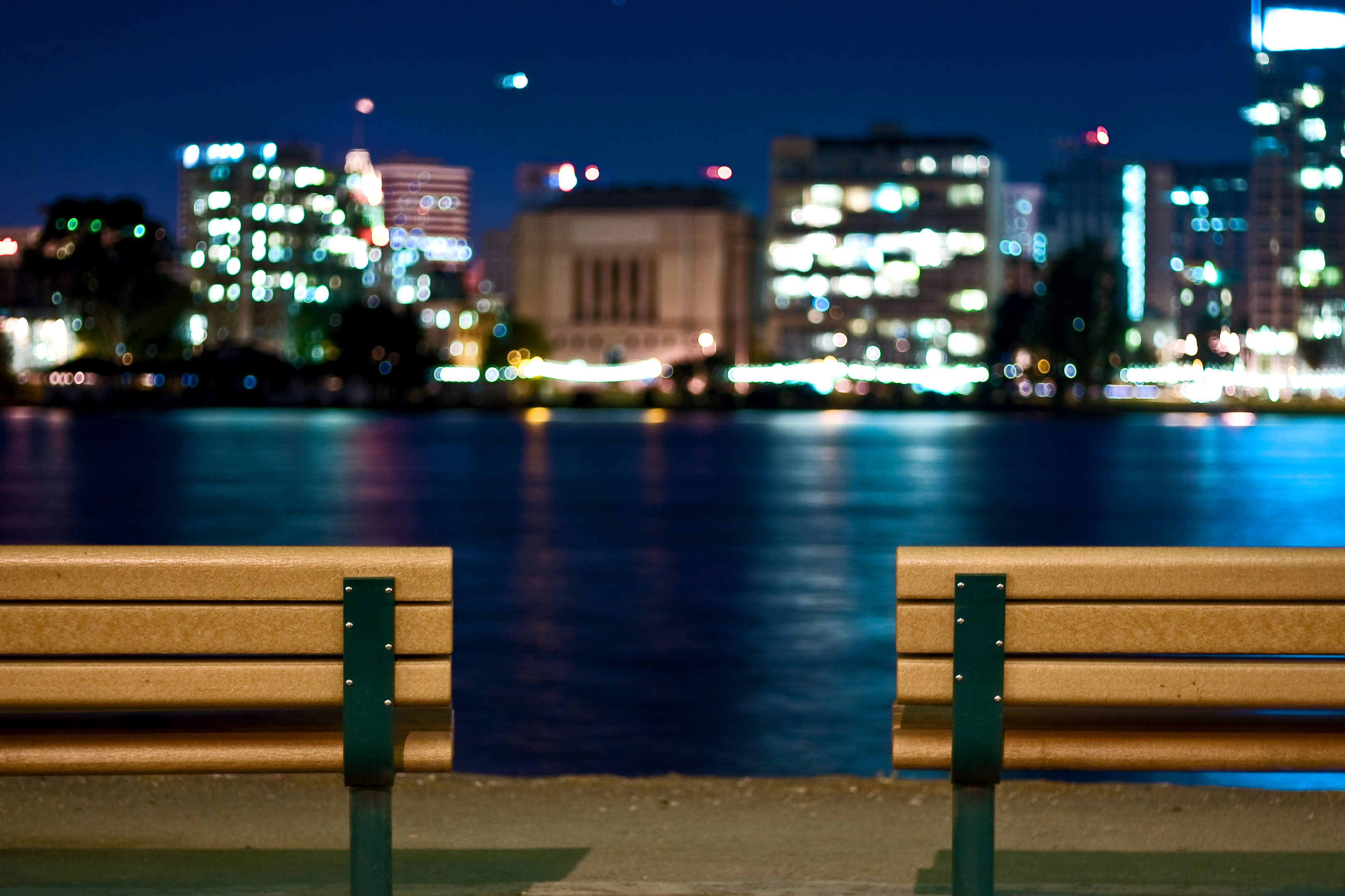 Lit benches overlooking city and body of water at night.