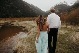 Couple holding hands walking towards mountains.