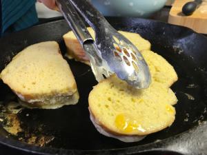 Pair of tongs grabbing one of several sandwiches off cast iron griddle