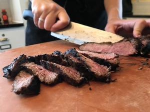Hands slicing juicy, medium-rare-prepared grilled meat on countertop