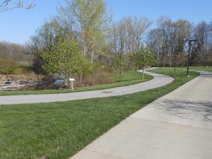 The sidewalk meanders from smooth, flat grass to wooded areas.