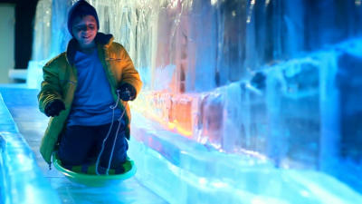 a boy sledding down an colorfully lighted ice slide