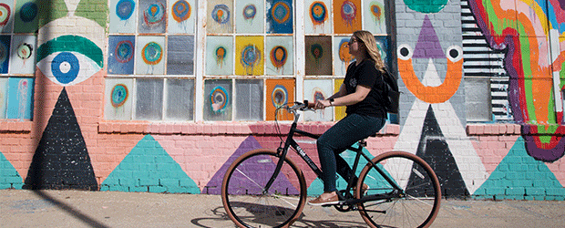 Girl riding bike in front of colorful mural