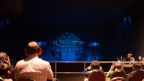 a faraday cage sits on a stage surrounded by giant Telsa coils