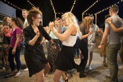 Two young women dancing with crowd of people under fairy lights