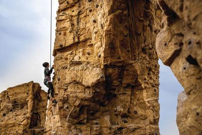 Woman in climbing gear hanging from wires and climbing up on climbing wall at Scioto Audubon Metro Park