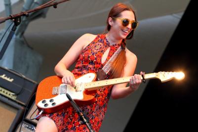 Musician Angela Perley playing guitar and smiling on stage during concert