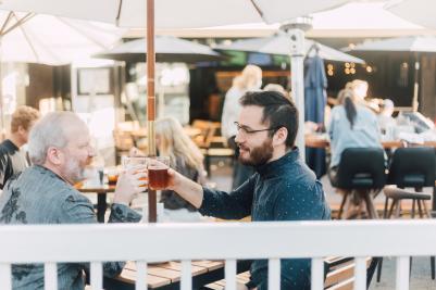 Two men raising their glasses to each other at an outdoor eating venue in SLO CAL