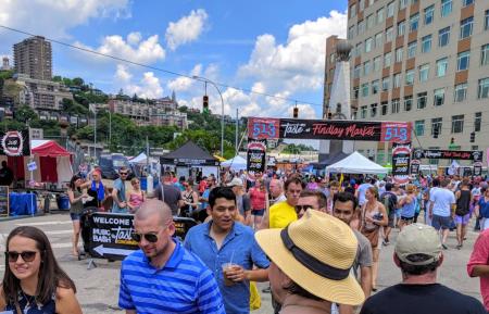 Taste of Cincinnati crowd in downtown Cincy headed under banner with blue sky and Mt. Adams in background