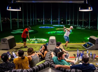Group of friends lounging on couches and hitting golf balls in hitting bay at Topgolf