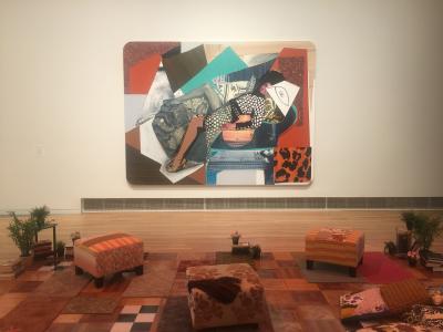 Large collage by Mickalene Thomas picturing a lounging woman, hung in a room with white walls and vibrant, modern furniture