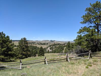 A log fence overooks rolling hills and mountain ranges as the land slopes down into canyons and hills outside Albin, Wyoming, used for cattle pasture land.