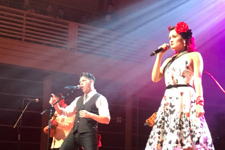Chicano-rockabilly band Las Cafeteras - a woman in a white dress and a man in a dark vest sing on stage at Green Music Center in Sonoma