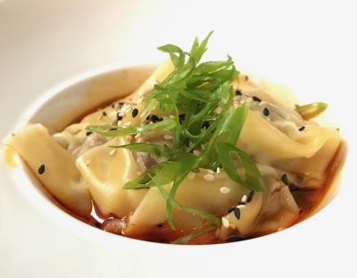 Bowl of dumplings in red sauce topped with greens and black seeds at Service Bar