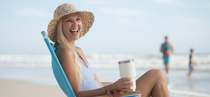 A woman enjoys a cup of coffee while sitting at the beach.