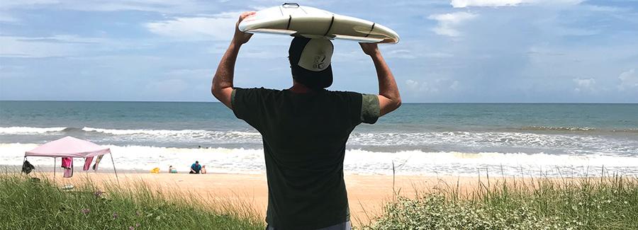 A surfer eyes the waves while a family enjoys their Daytona Beach day