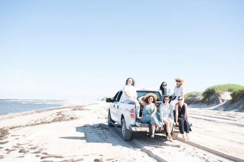 A group of visitors ride down the beach in the bed of a 4x4 truck.