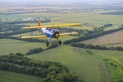 Blue and yellow plane flying over Kansas countryside