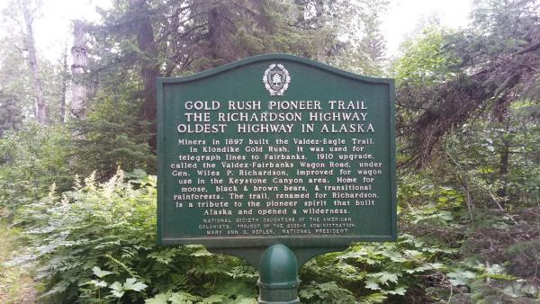 a sign for the Gold Rush Pioneers Trail in Valdez, Alaska. Trees in background