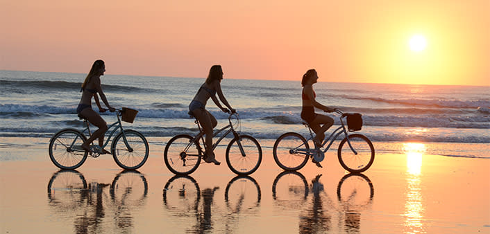 A group of female friends enjoy a sunrise bicycle ride on the beach