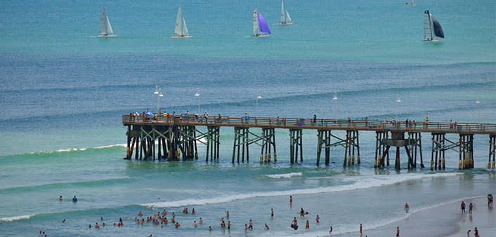 Daytona Beach Pier is a picturesque spot with people fishing, beach goers and sail boats on the horizon