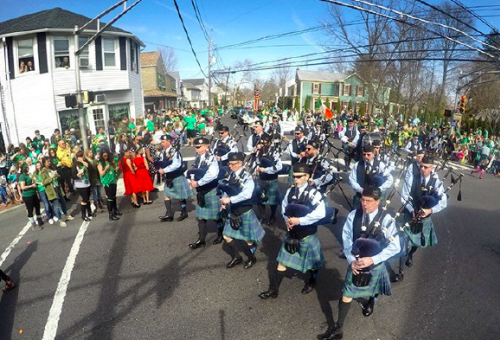 A marching band of the celtic variety walking up the street during a parage all holding bagpipes