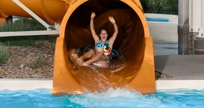A girl gets ready to exit a water slide into a pool while riding an inflatable tube at the Wichita YMCA