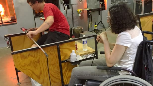 A young woman in a manual wheelchair blowing glass at the Corning Museum of Glass
