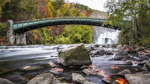 A view of a bridge and water flowing on rocks with the New Croton Dam waterfall in the background