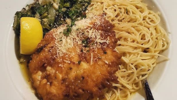 A photo of chicken French with spaghetti a lemon wedge and spinach