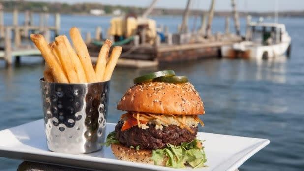 A burger and fries pictured on the waterfront with a boat in the background